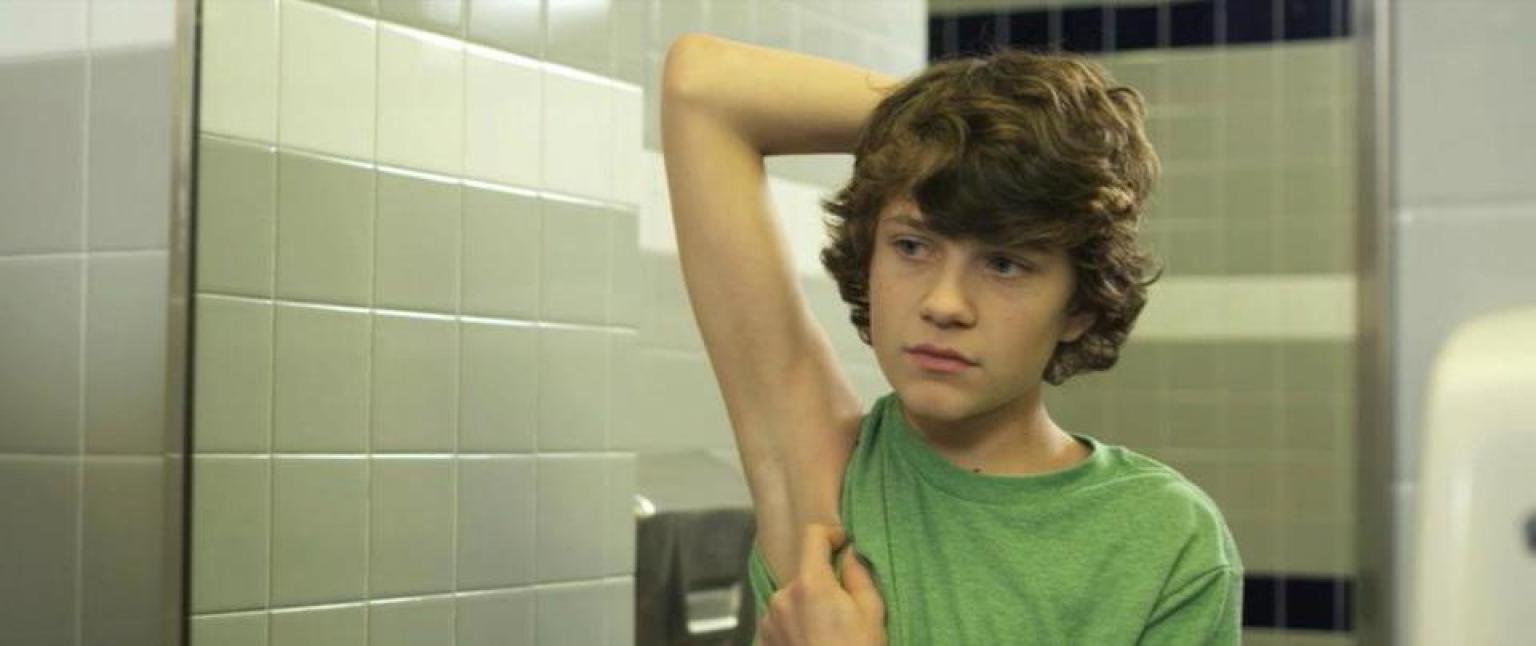 Curly haired brunette twelve year old boy looking in mirror at his raised a...